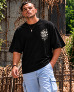 Model wearing black MUD BREAK THROUGH Monochrome Tee, front view with small monochrome Man Up Differently chest graphic